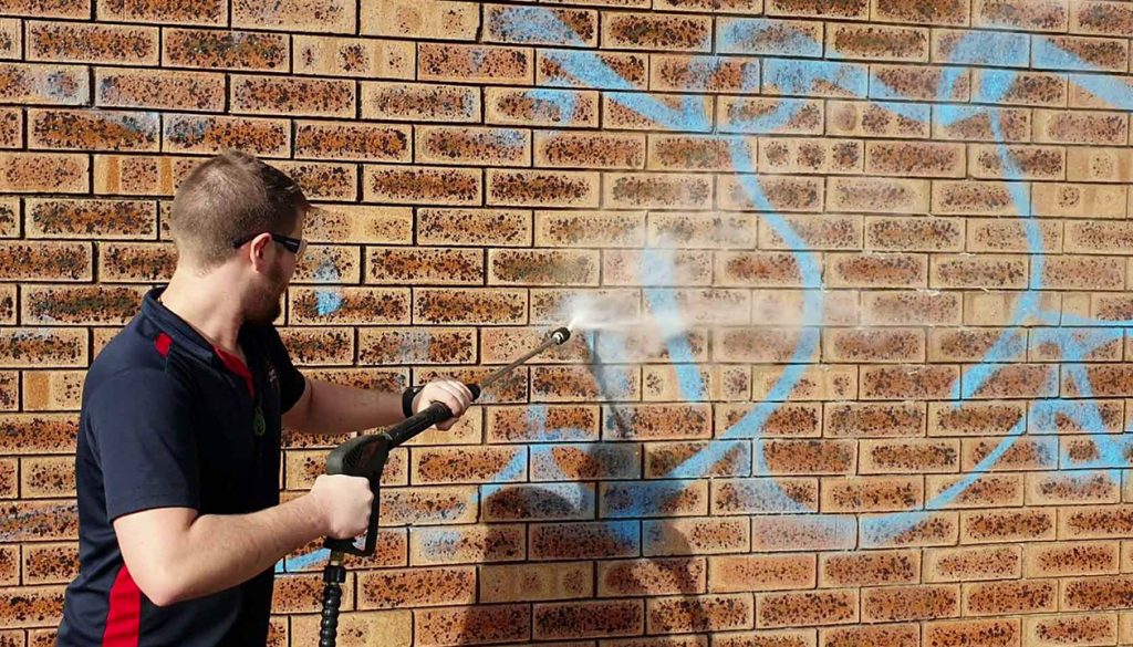 Man pressure washing graffiti wall